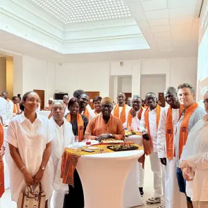 Groupe de personnes en tenue blanche avec des &eacute;charpes orange autour d'une table.