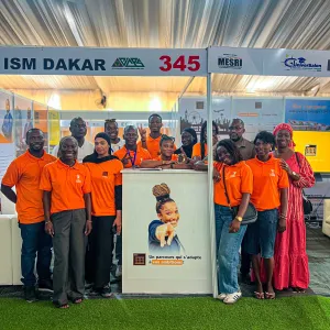 Groupe de personnes en t-shirts orange posant autour d'un portrait, stand ISM Dakar.