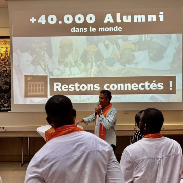 Photographie d'un homme donnant une pr&eacute;sentation, public v&ecirc;tu de blanc.